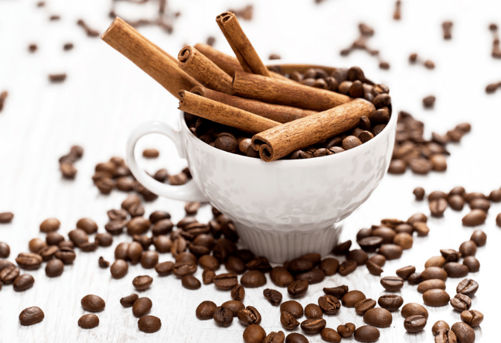 Cinnamon sticks and coffee beans in a white cup