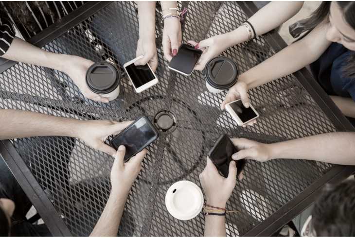 Friends at coffee shop checking social media on their phones