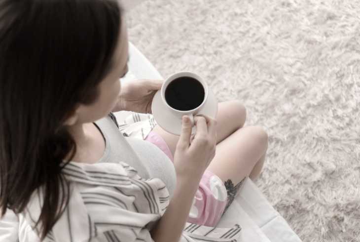 Pregnant woman sitting on the edge of bed drinking coffee