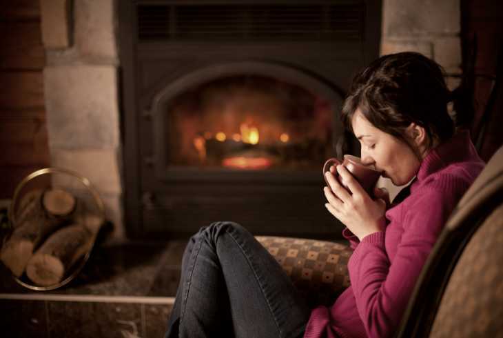 Young woman enjoying a coffee by a cozy fire